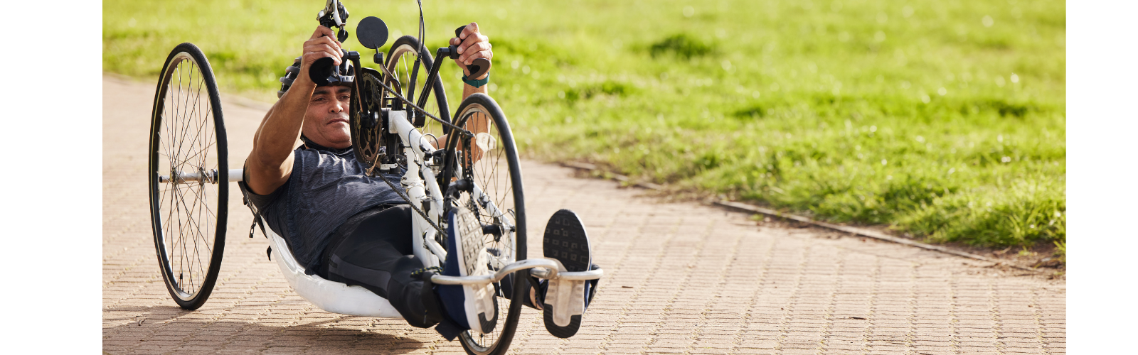 A man is riding a specially designed bicycle with hand pedals across a stone path. 
